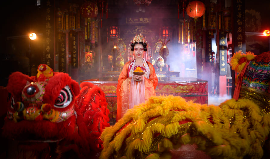 Mujer vestida con traje tradicional chino sosteniendo una ofrenda junto a disfraces de leones en un templo